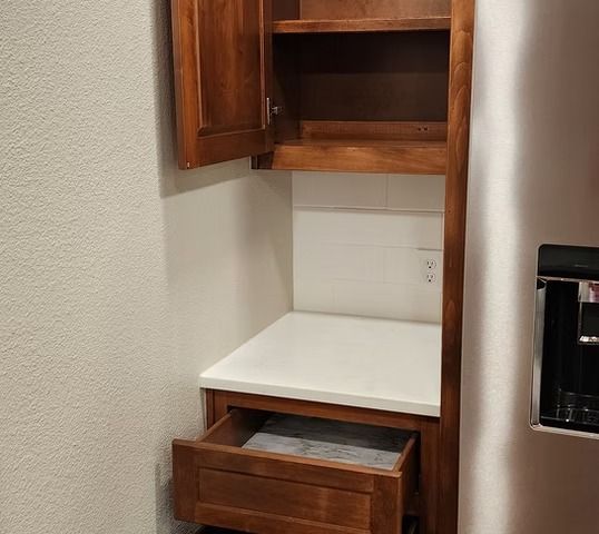 Built-in wooden kitchen cabinet with an open door, drawer, and countertop.