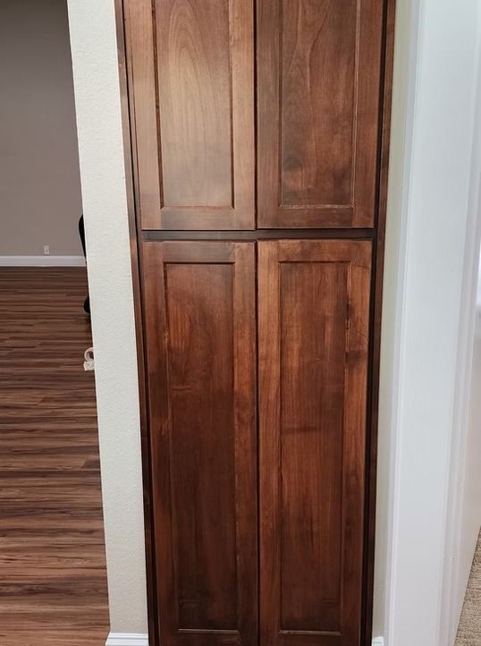 Tall, dark-stained wooden pantry cabinet built into a wall, with four door panels, in a home interior.