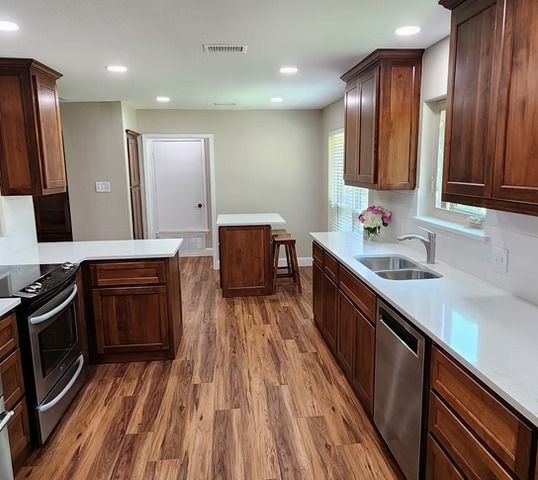 Kitchen with wood cabinets, white countertops, stainless steel appliances, and wood flooring.