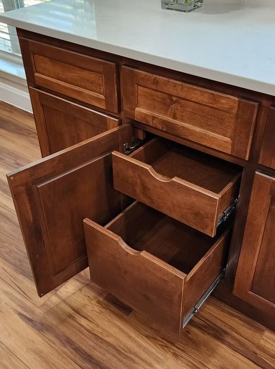 Wooden kitchen drawers partially opened, showing two pull-out drawers. Brown cabinets with a white countertop.