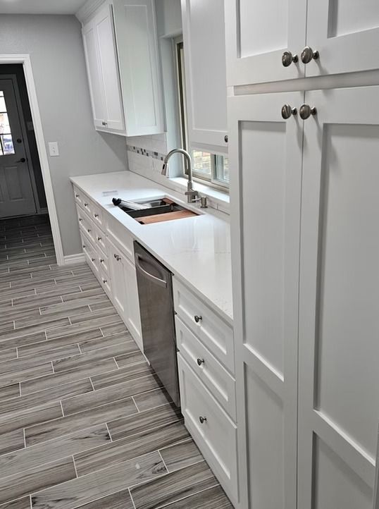 White kitchen with quartz countertops, stainless steel appliances, and gray tile flooring.