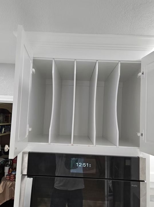 White kitchen cabinet with dividers above a black oven.