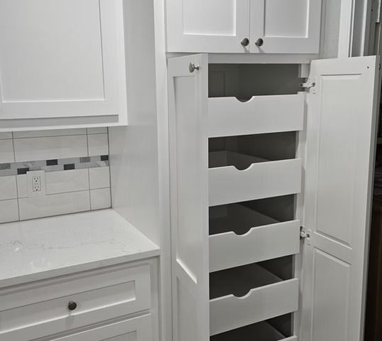 White kitchen cabinet with pull-out drawers, door open. Quartz countertop and backsplash in view.