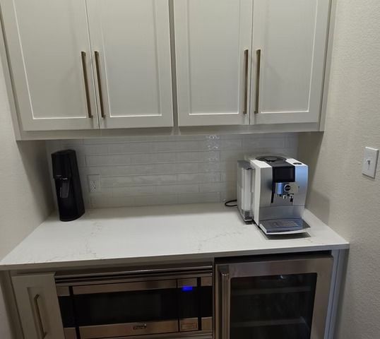 Built-in coffee station: white cabinets, quartz countertop, espresso machine, microwave, wine fridge.