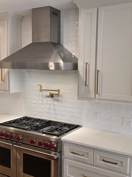 Stainless steel range hood above a gas range in a white kitchen with white cabinets.