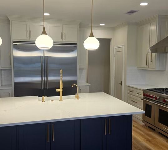 Modern kitchen with blue island, white countertops, stainless steel appliances, and gold fixtures.
