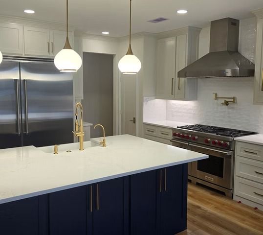 Modern kitchen with white countertops, blue island, stainless steel appliances, and gold fixtures.