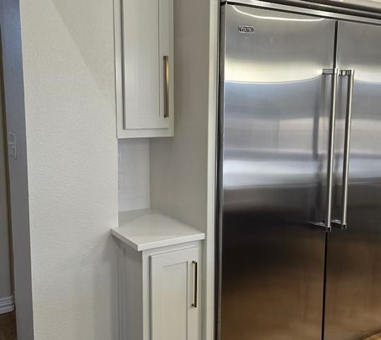 White kitchen cabinets and countertop next to a stainless steel refrigerator.