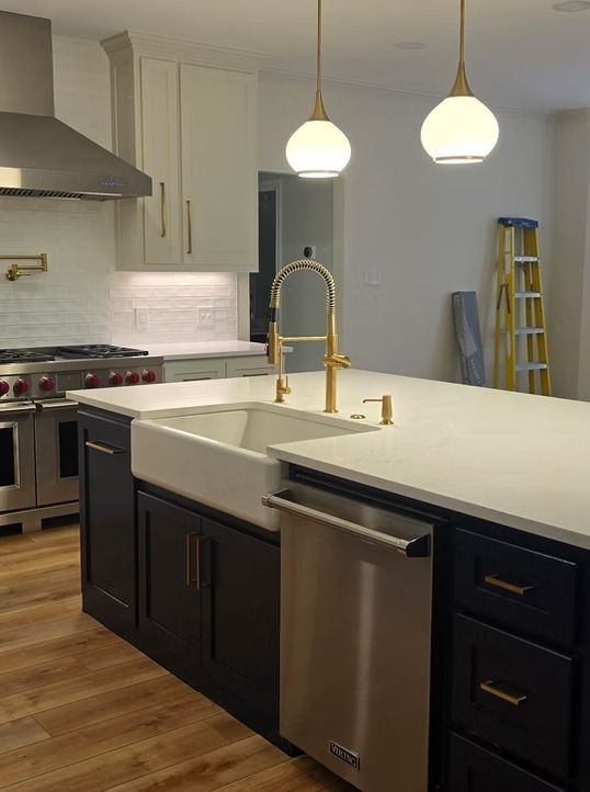 Kitchen with navy island, white countertops, gold fixtures, white cabinets, and stainless steel appliances.
