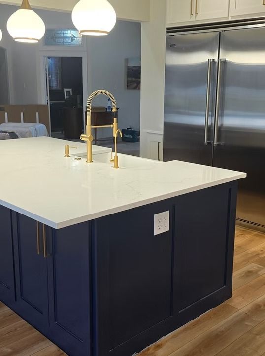 Navy blue kitchen island with white countertop, gold faucet, and stainless steel refrigerator.