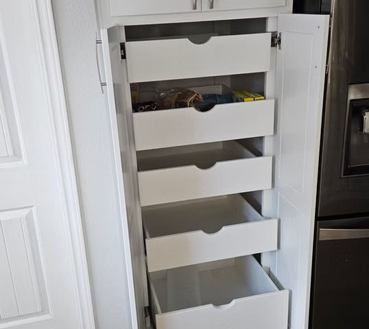 White kitchen pantry with pull-out drawers, partially open, against a refrigerator.