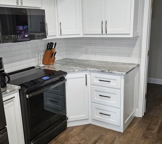 White kitchen with stove, cabinets, and granite countertop.