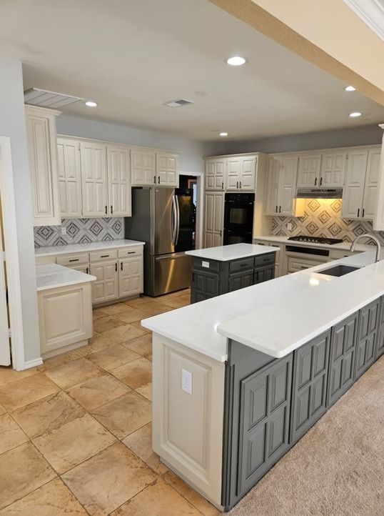Spacious kitchen with cream and gray cabinets, two islands, stainless steel appliances, and tiled backsplash.