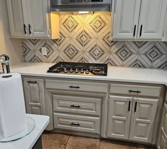 Kitchen with light-colored cabinets, white countertops, a gas cooktop, and patterned tile backsplash.