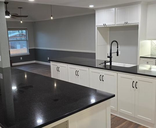 Modern kitchen with white cabinets, black countertops, and grey walls.
