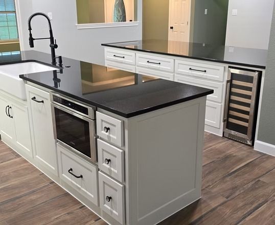 White kitchen island with black countertop, sink, oven, and wine cooler.