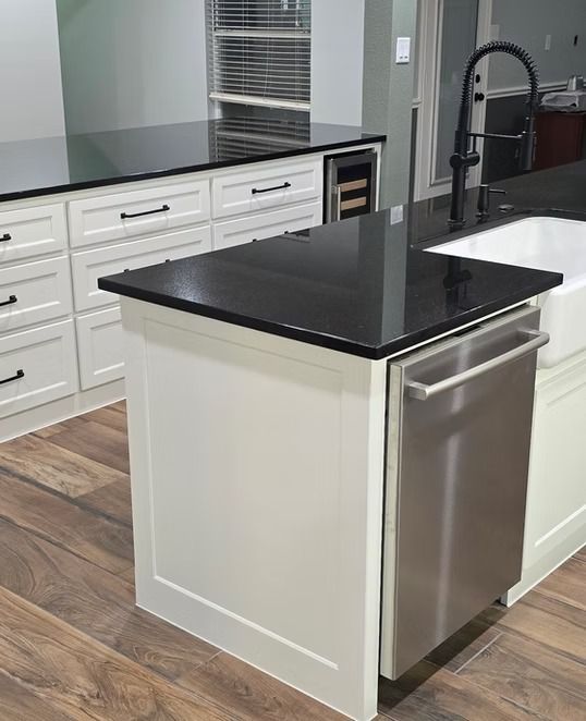 Kitchen island with a black countertop, white cabinets, and a stainless steel dishwasher.