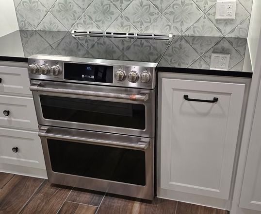 Stainless steel double oven in a kitchen with white cabinets and patterned backsplash.