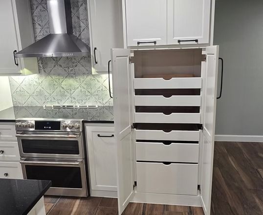 White kitchen pantry with pull-out drawers, open. Stainless steel appliances and tile backsplash visible.