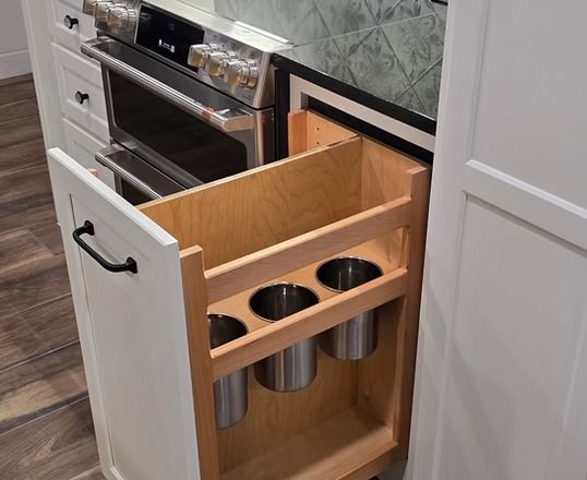 A pull-out kitchen cabinet with stainless steel utensil holders beside an oven.