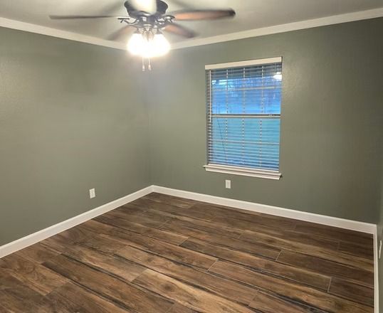 Empty bedroom with olive-green walls, wood-look flooring, ceiling fan, and a window with blinds.
