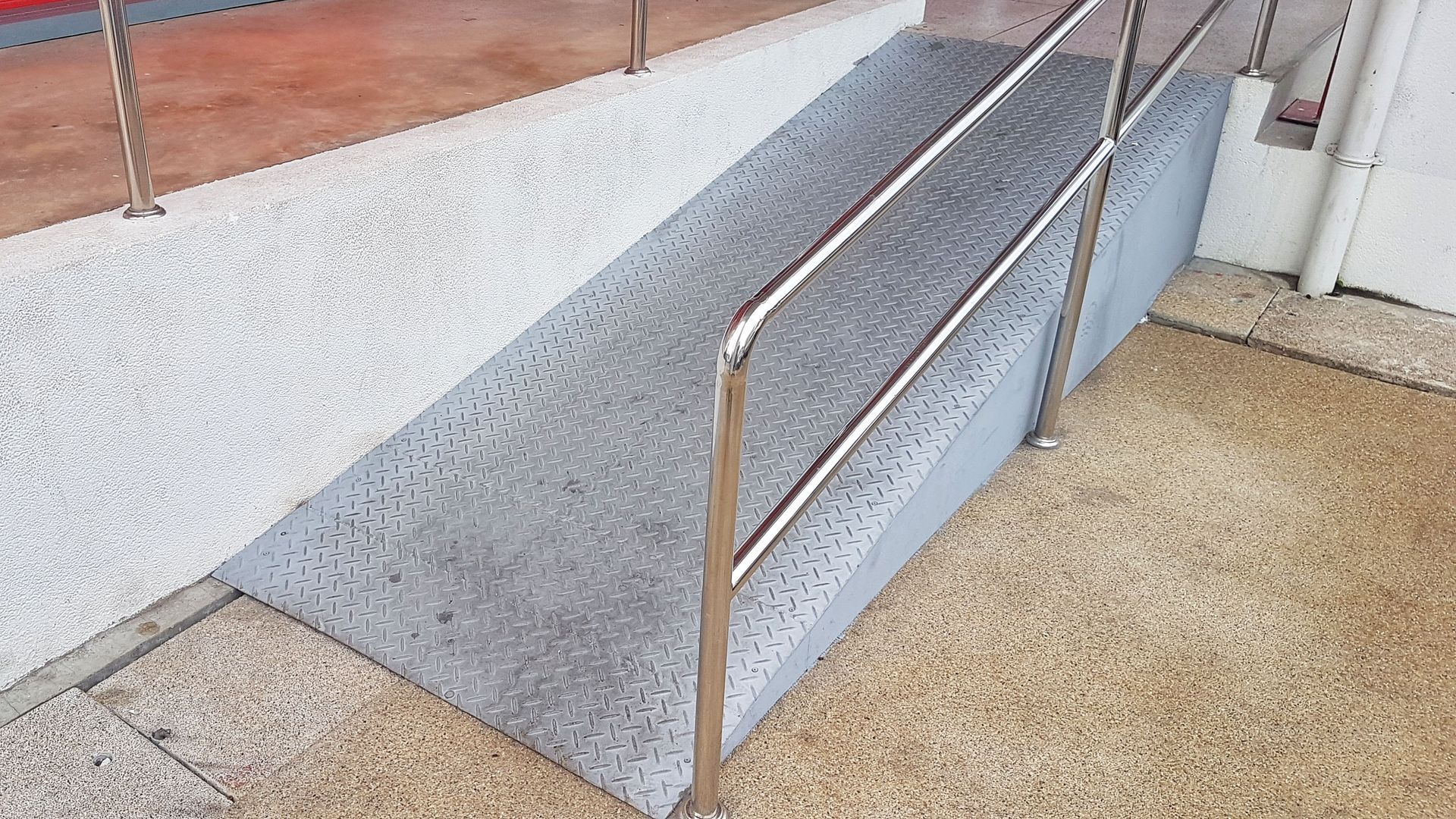 Ramp with metal handrails provides accessibility to a higher level. Textured concrete.