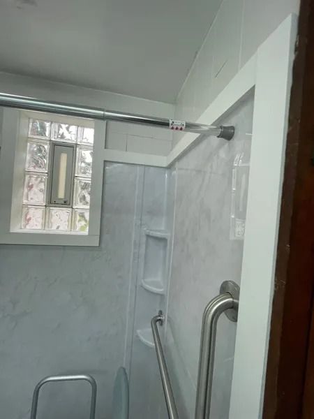 White accessible shower with grab bars and built-in soap dish. Window with glass blocks visible.