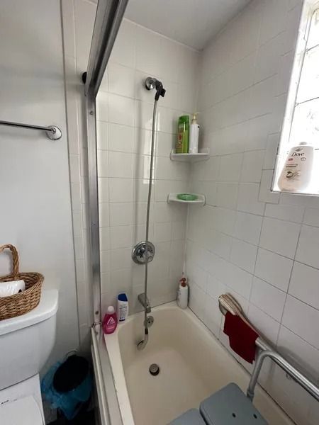 Bathroom with bathtub, shower head, white tiled walls, and grab bar.