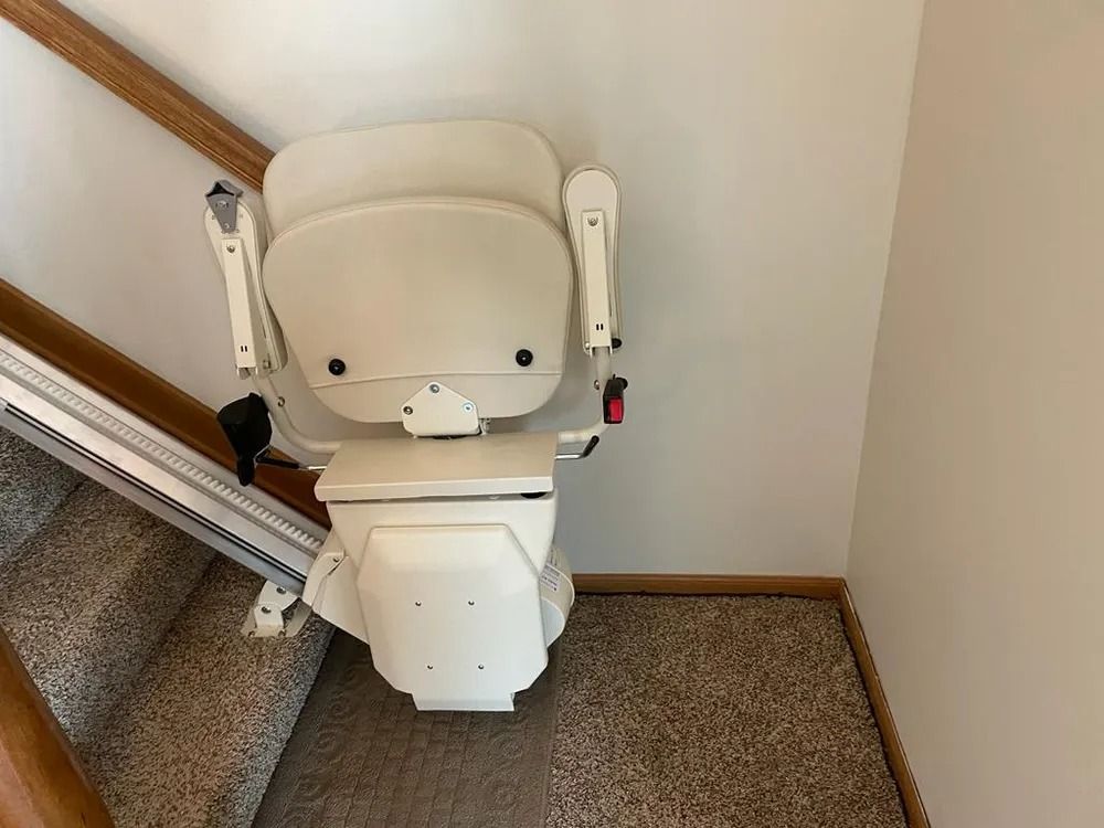Stair lift chair on a staircase. Beige chair, rail and wall, brown carpet, descending.