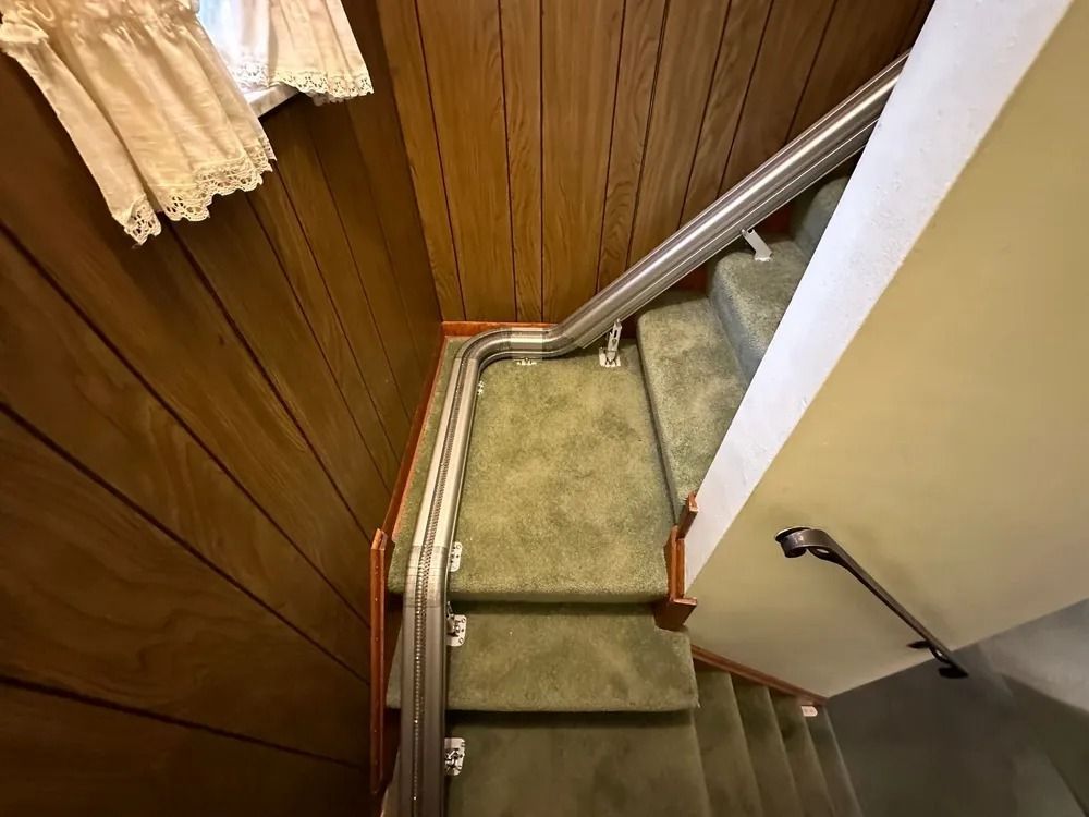 Staircase with green carpet and wooden paneling, a handrail, and a curved section.