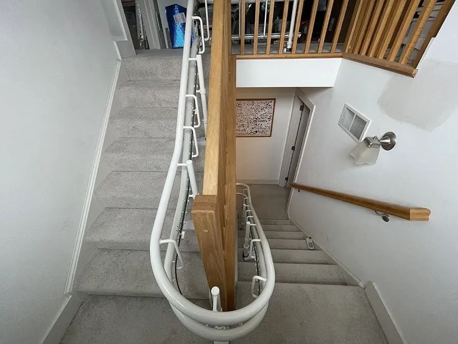 Staircase with white railing curving down, brown wooden newel post, carpeted steps, and doorway at the bottom.