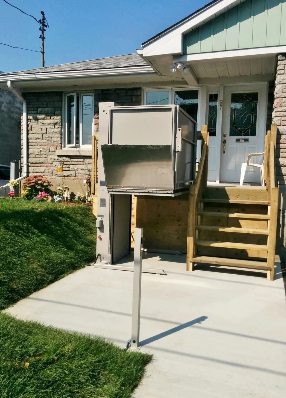 Exterior view of a home with a platform lift installed, providing accessible entry. Concrete path, stairs, and green lawn.