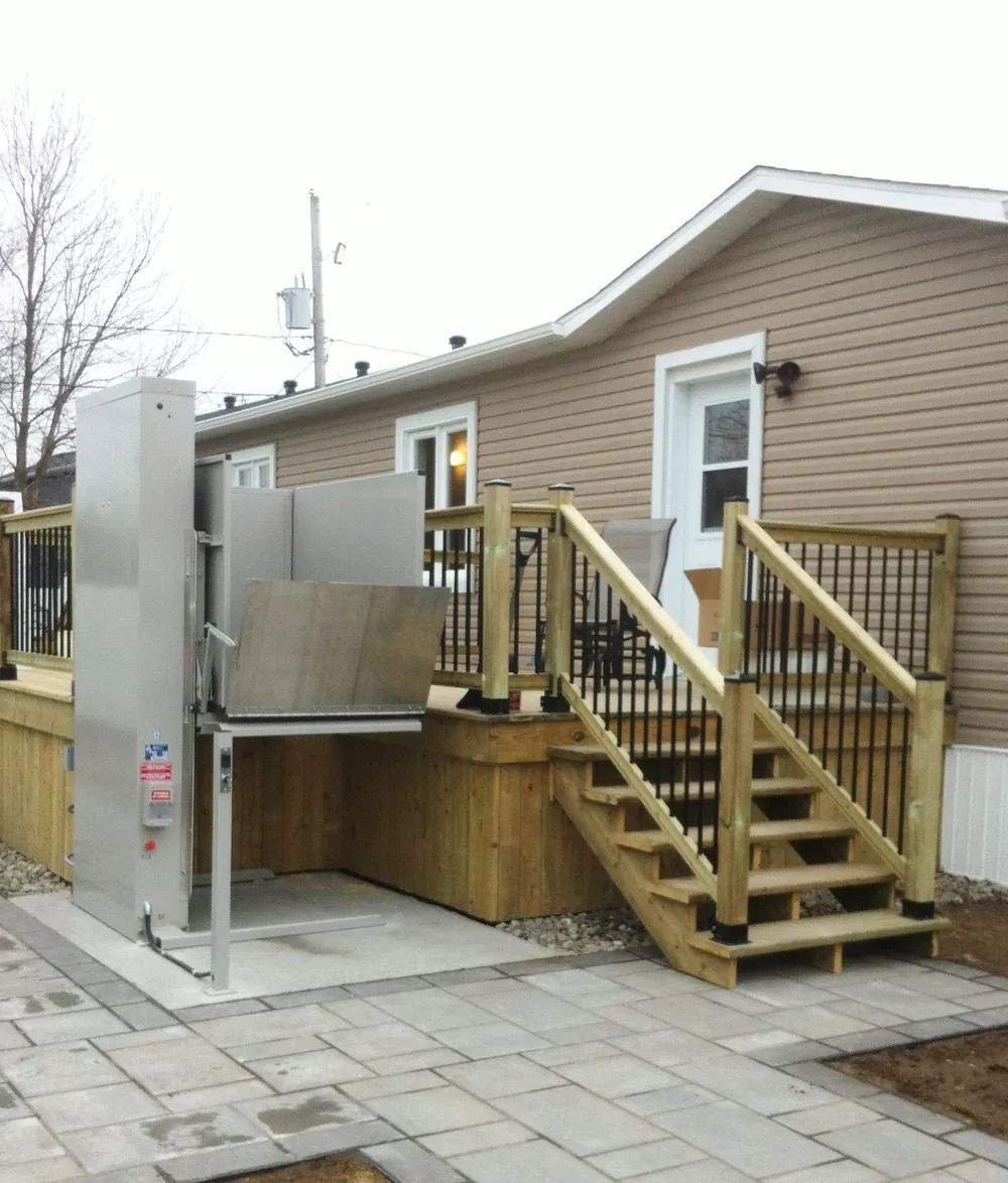 Outdoor wheelchair lift next to a house with wooden deck and stairs.