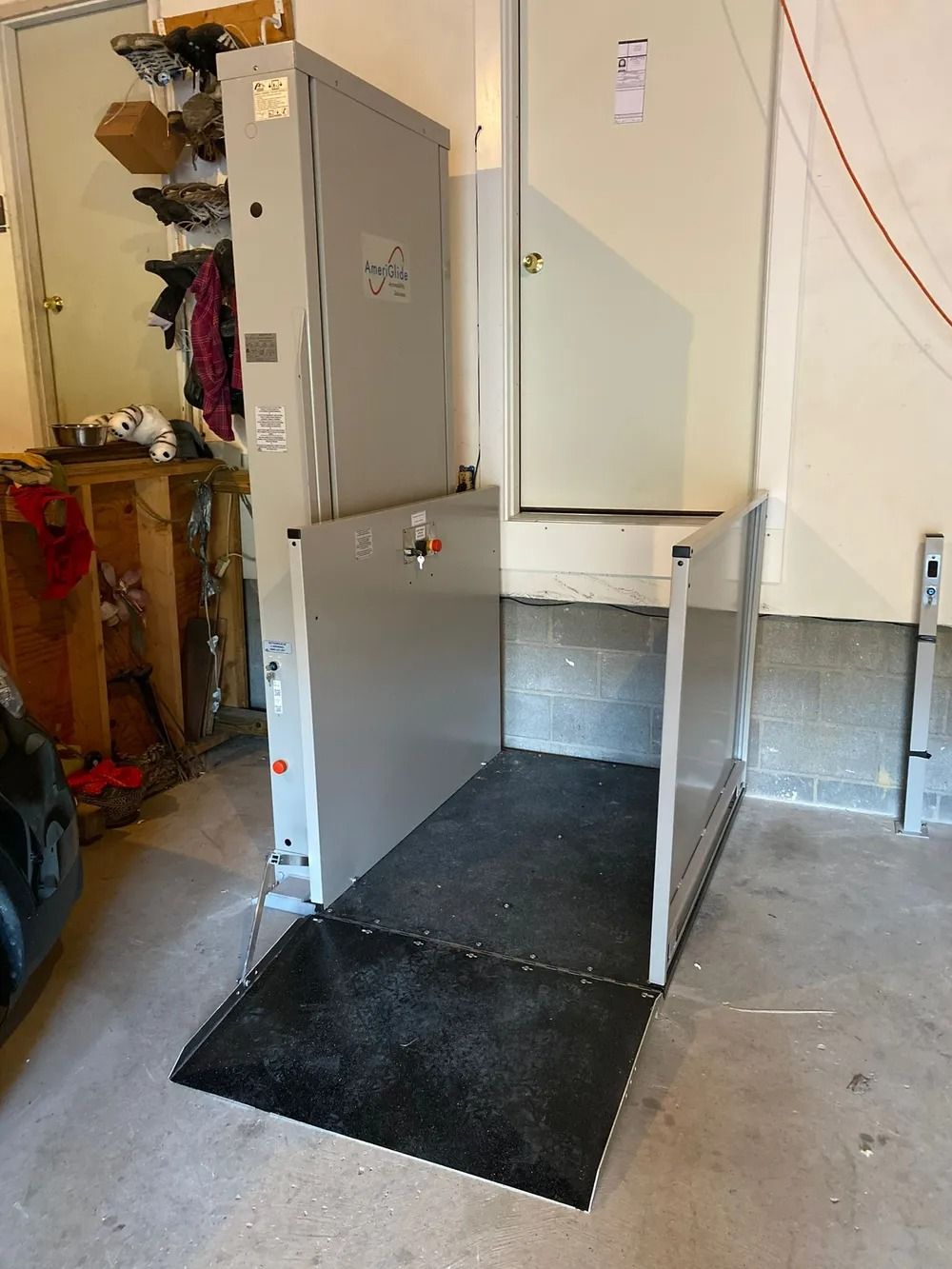 Platform lift in a garage, gray metal with black non-slip surface, for wheelchair accessibility.