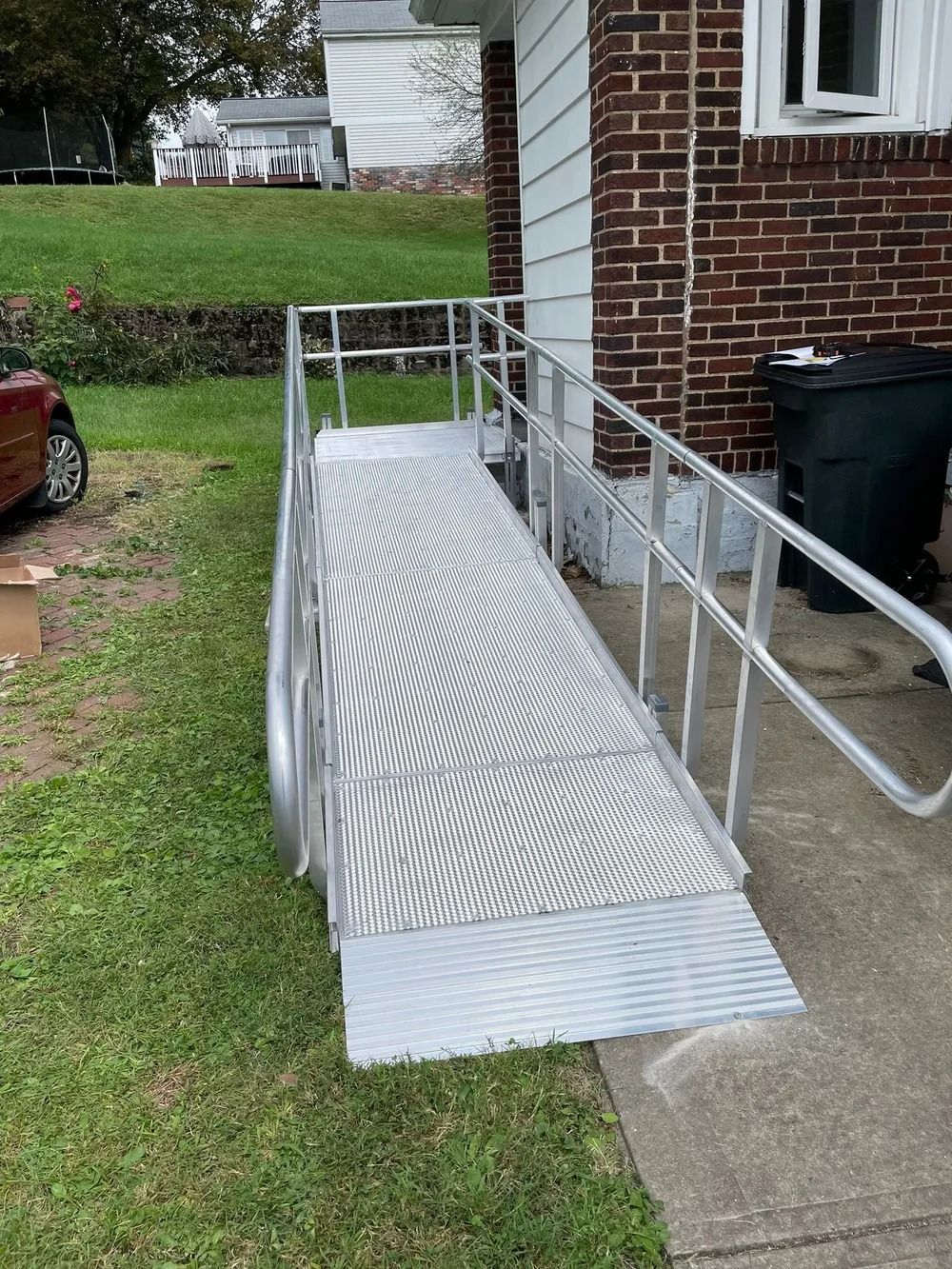 Aluminum ramp with handrails providing accessible entry to a brick house, on a grassy lawn.
