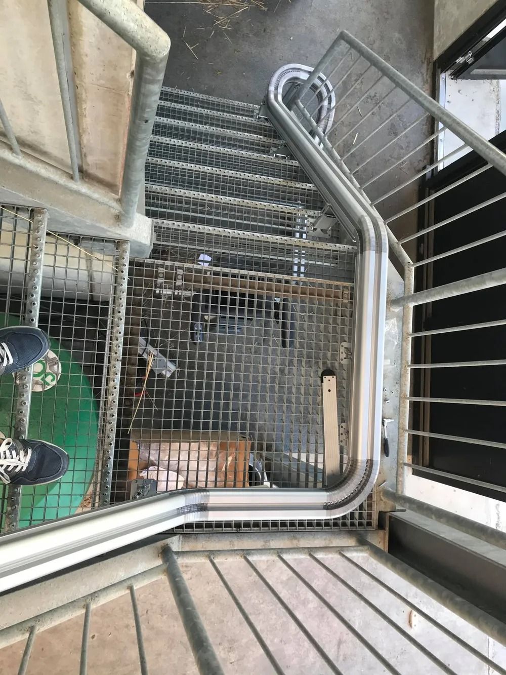 Metal stairs with handrails and a grated landing. Feet are visible at the bottom.
