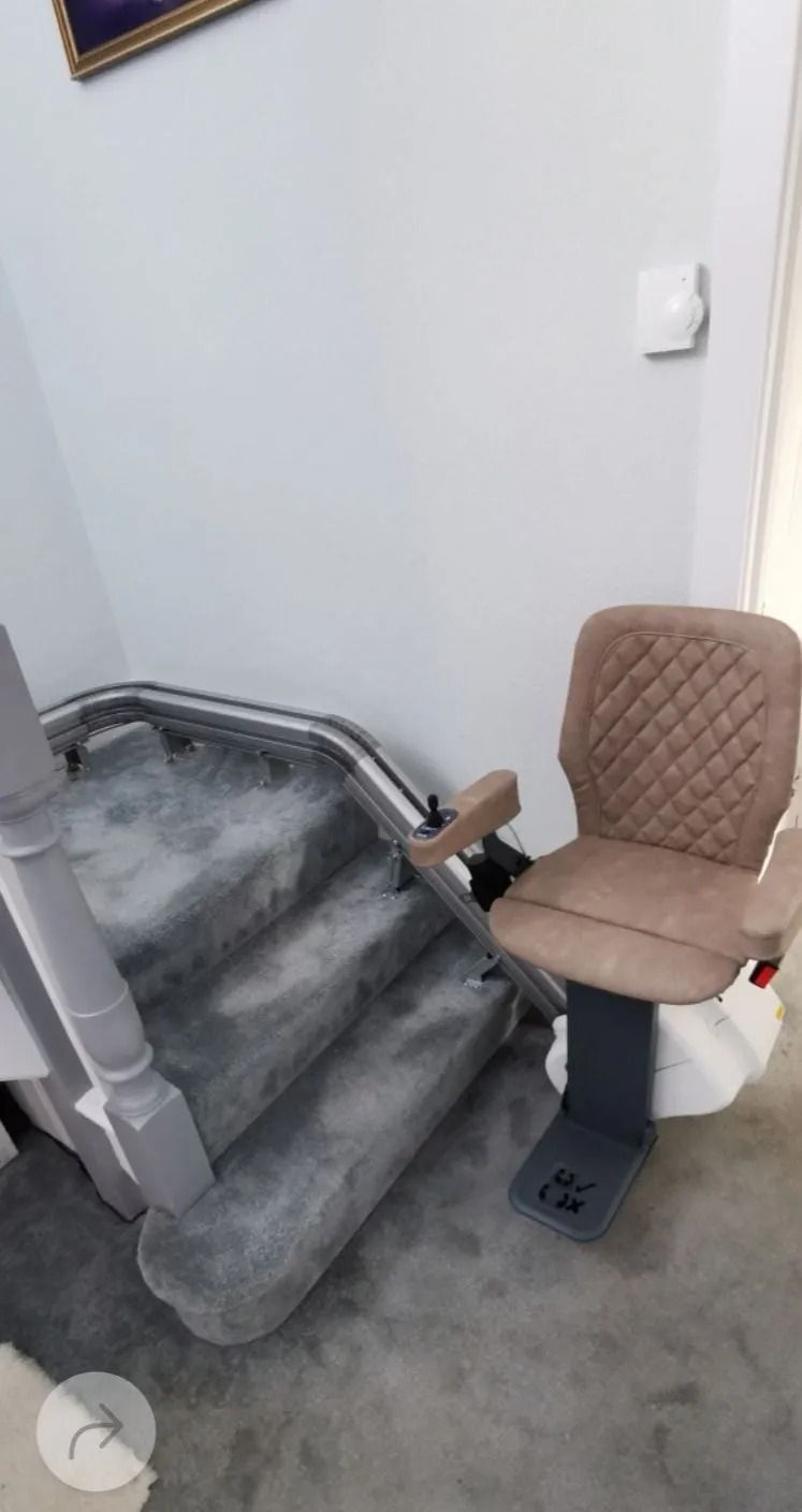 Stair lift installed on a carpeted staircase. The lift has a brown quilted seat and gray base.