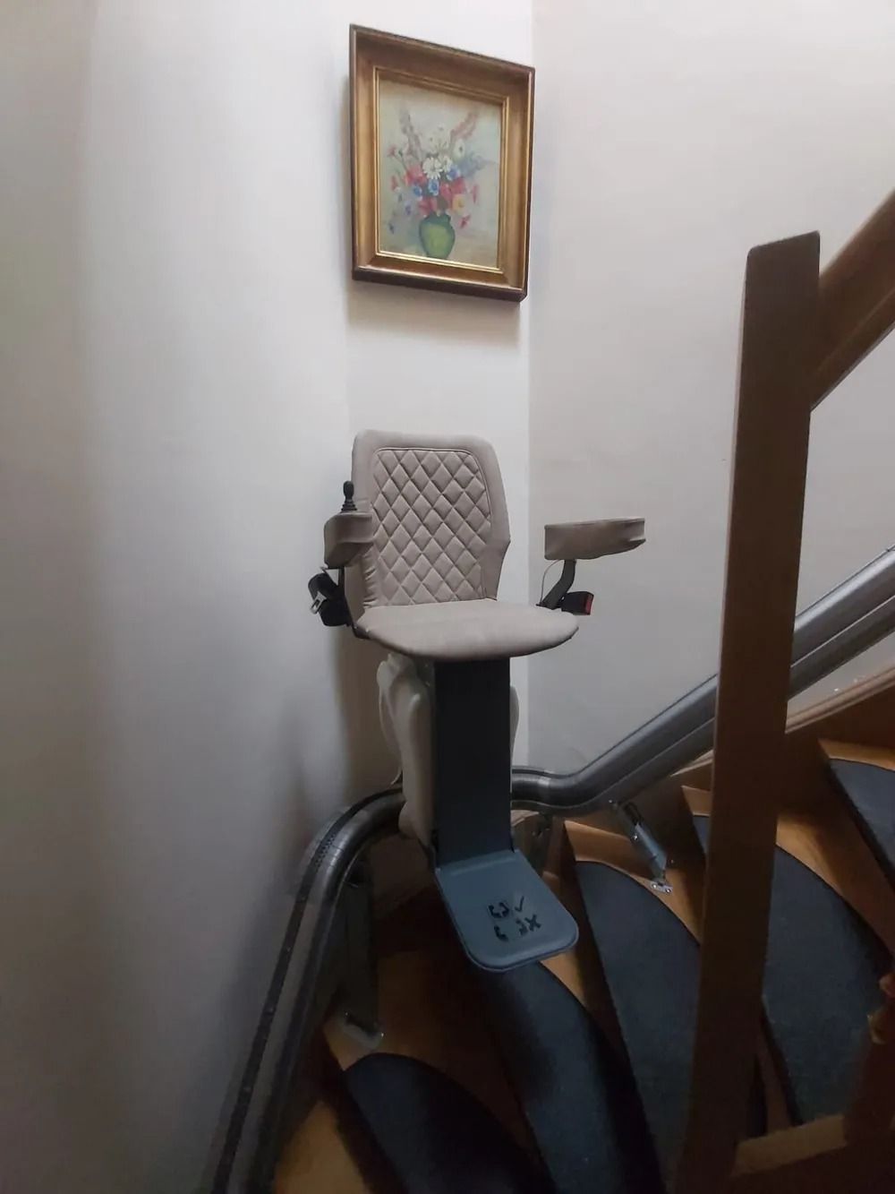 Stair lift installed on a wooden staircase with a painting on the wall above it.