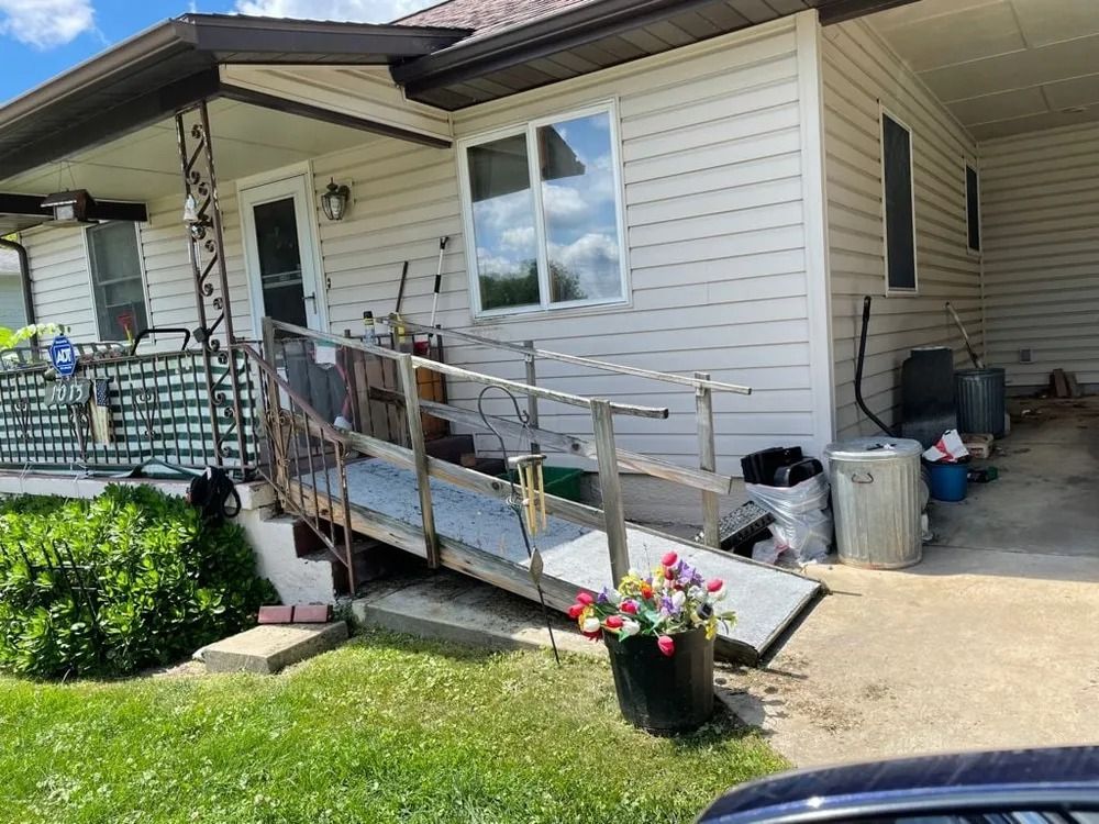 Ramp leading to a house entrance with white siding. Flowers in a pot are at the base of the ramp.