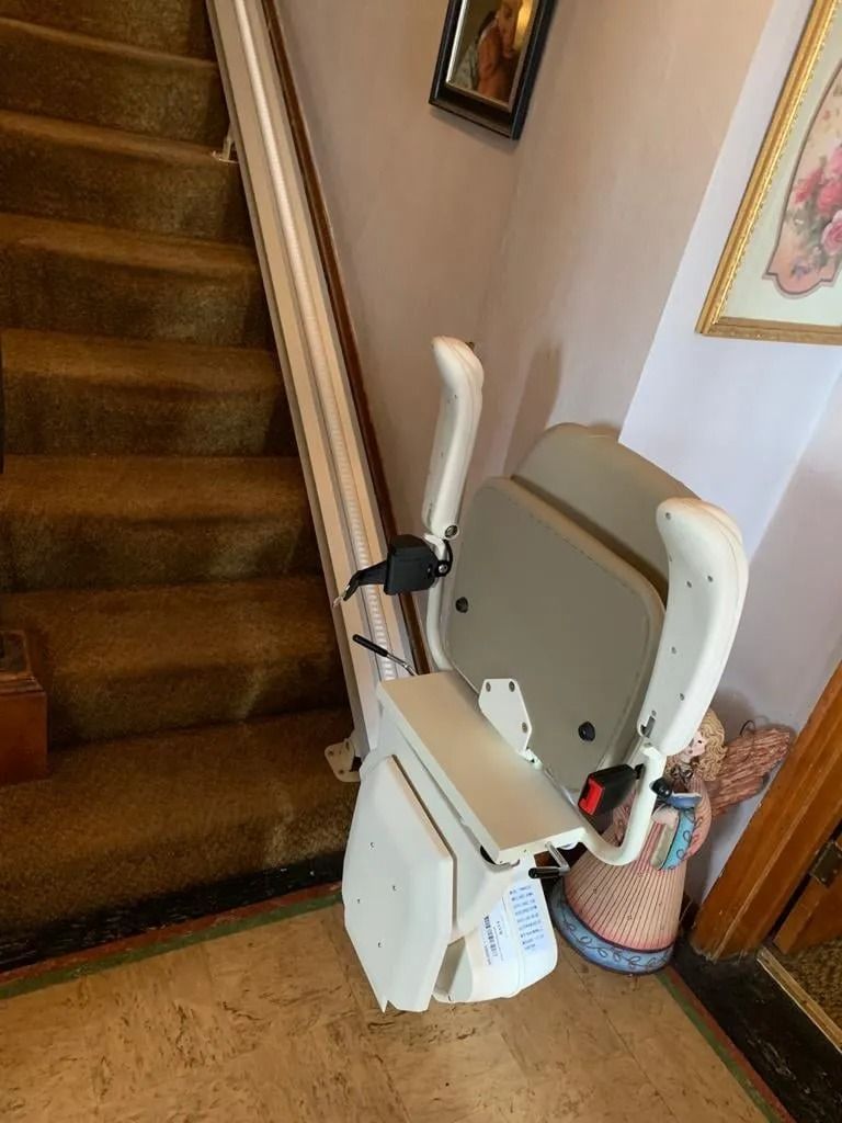 Stair lift installed on a staircase with beige carpet, white rail, and a light-colored seat.