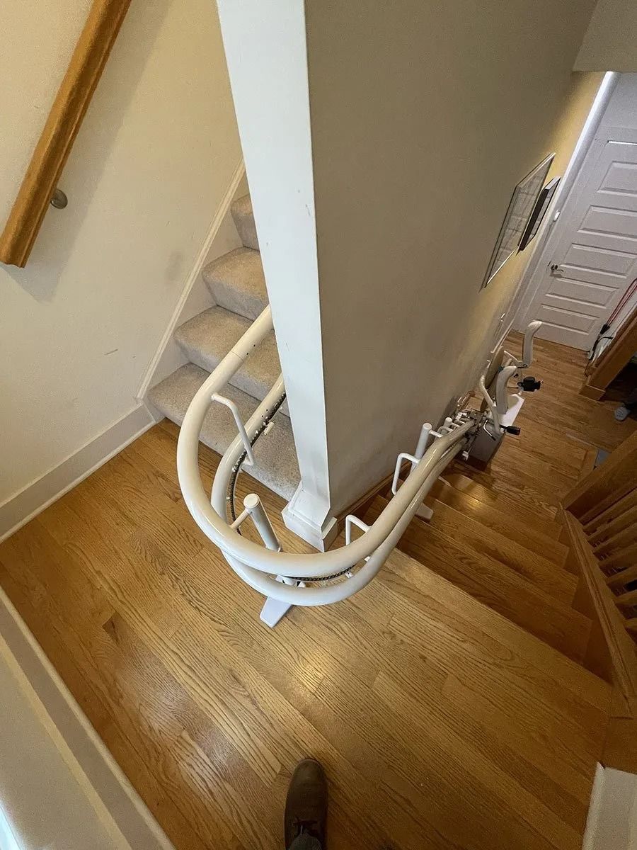 Stair lift on a wooden staircase with a wall separating the stairs. Beige and brown tones.