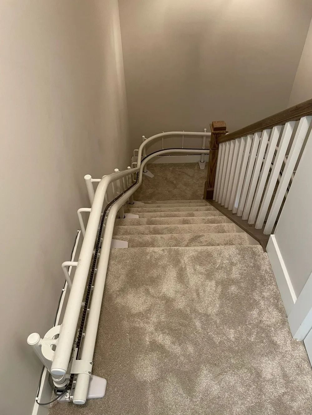 Staircase with a curved stair lift on the left side and a railing on the right, light tan carpet.