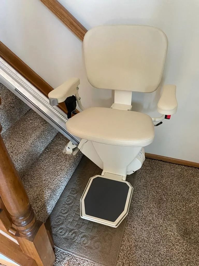 Beige stair lift chair on carpeted stairs.