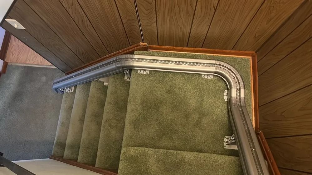 Staircase with curved, metal handrail on a green carpeted stairway. Wooden walls and ceiling.