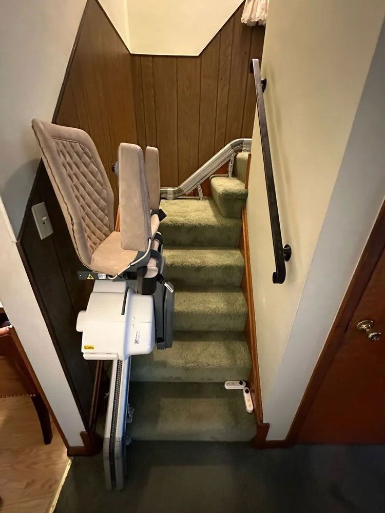Stairlift on a carpeted staircase with green carpet and wood paneling on the wall.
