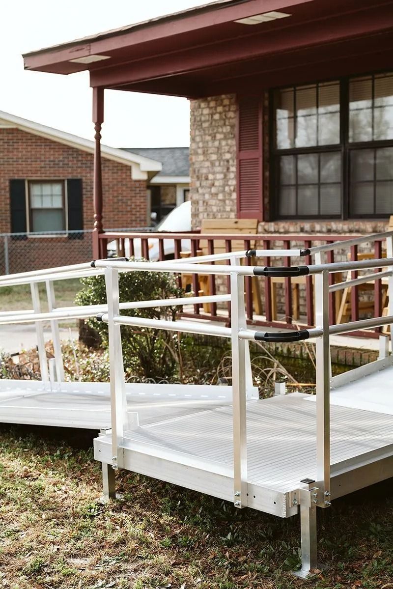 Metal wheelchair ramp leading to the porch of a brick house with a red roof.