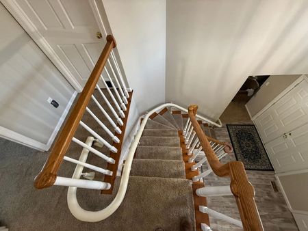Staircase with brown carpet and wooden handrails curving to the upper level.