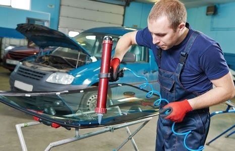 Mechanic applying sealant to a windshield in a garage.