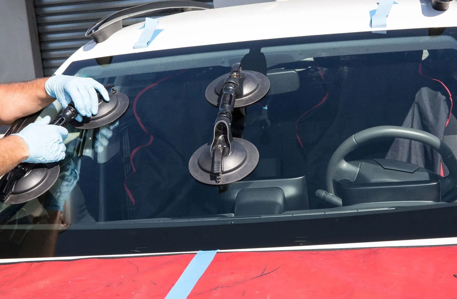 Hands in gloves using suction cups to remove a vehicle's windshield.