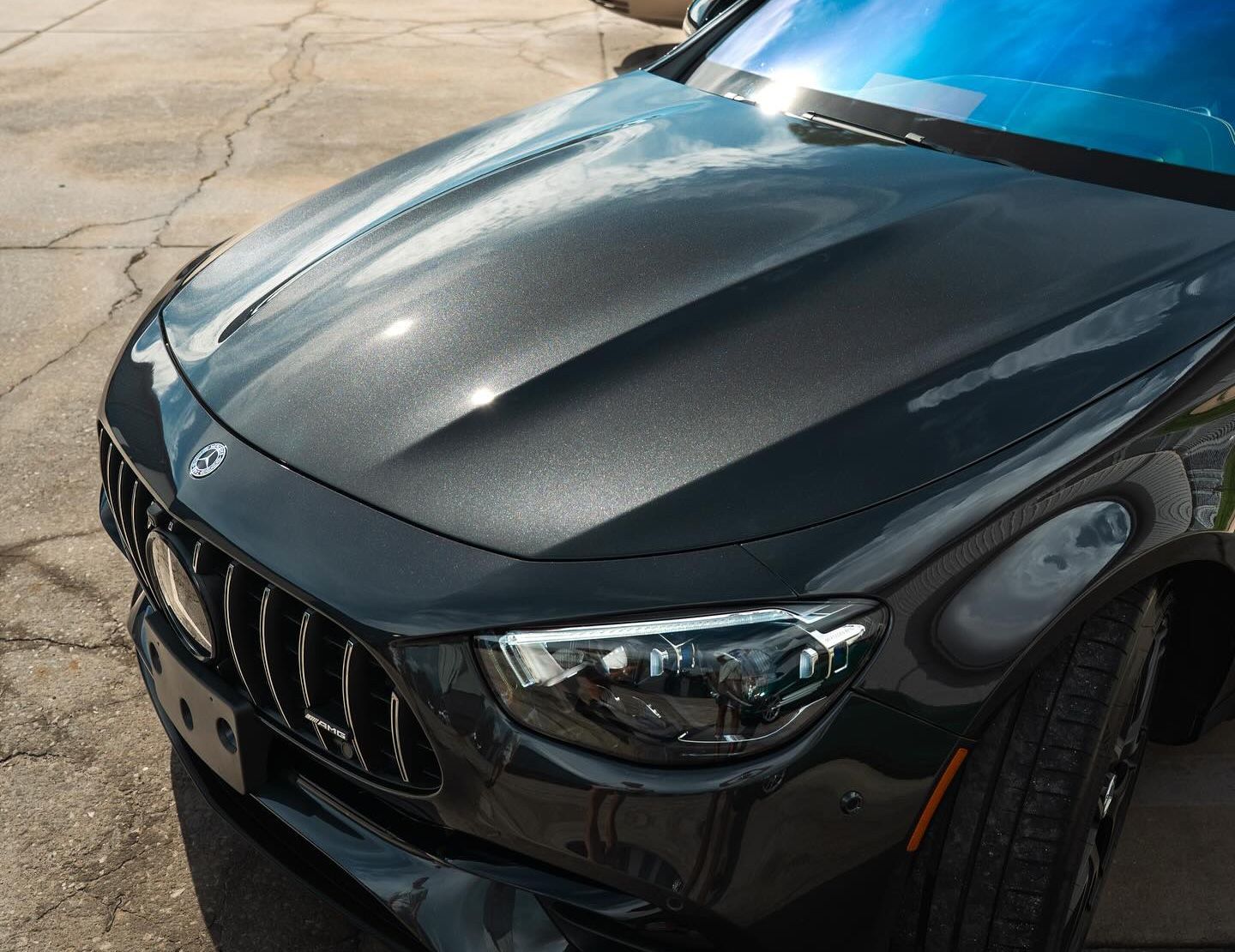 Dark gray Mercedes-Benz car hood, grill, and headlight, parked outdoors.